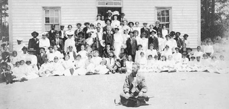 Black and white photo with superintendent in foreground and dozens of students and adults in background