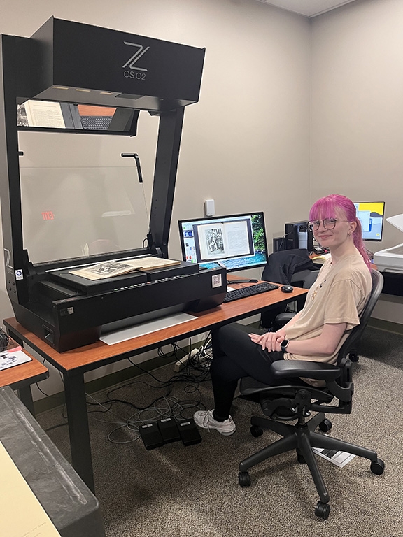 Image of student employee Madison Northup seated at book scanner. 